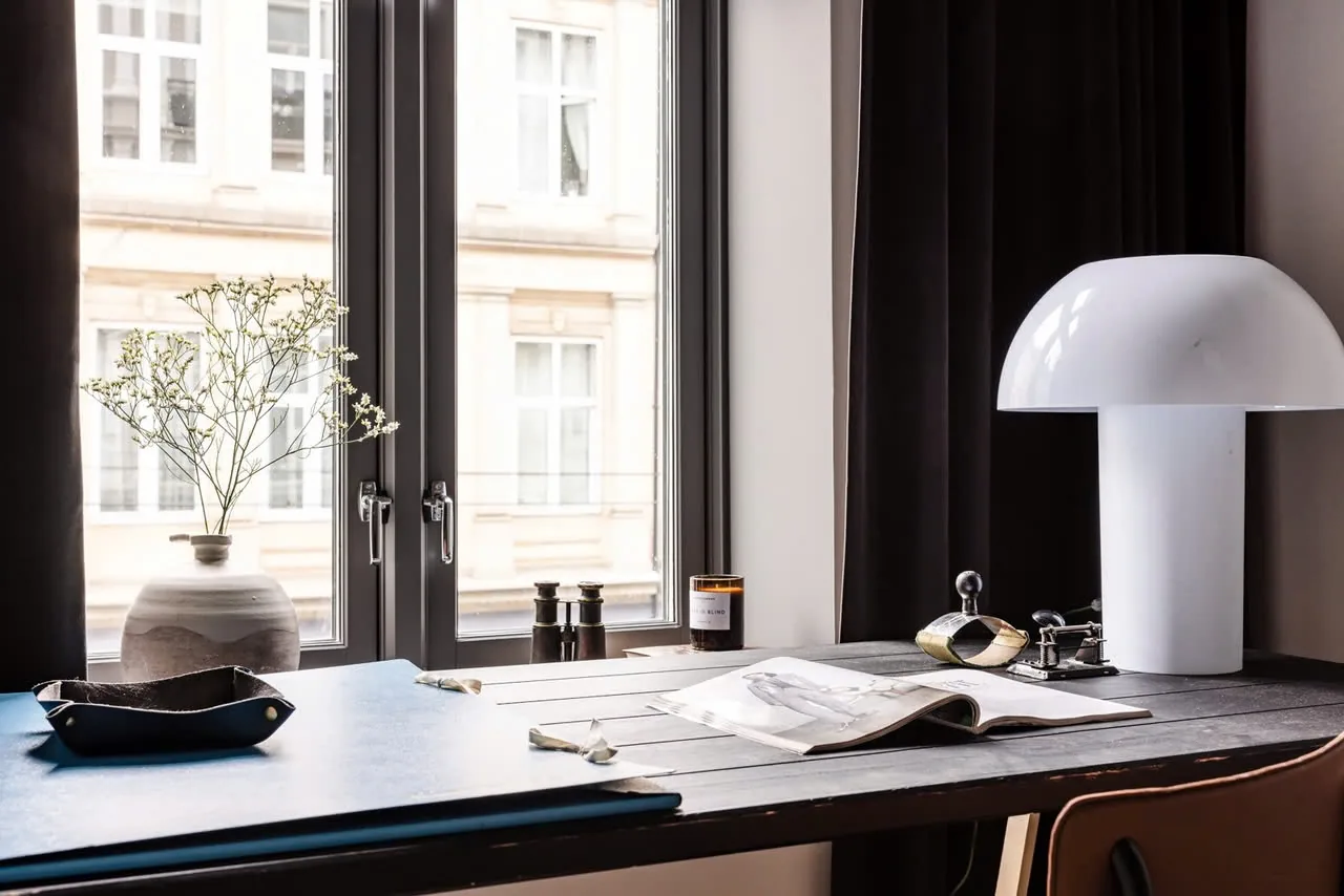 Skrivebordet med bordlampe og oppslått bok mot vinduet